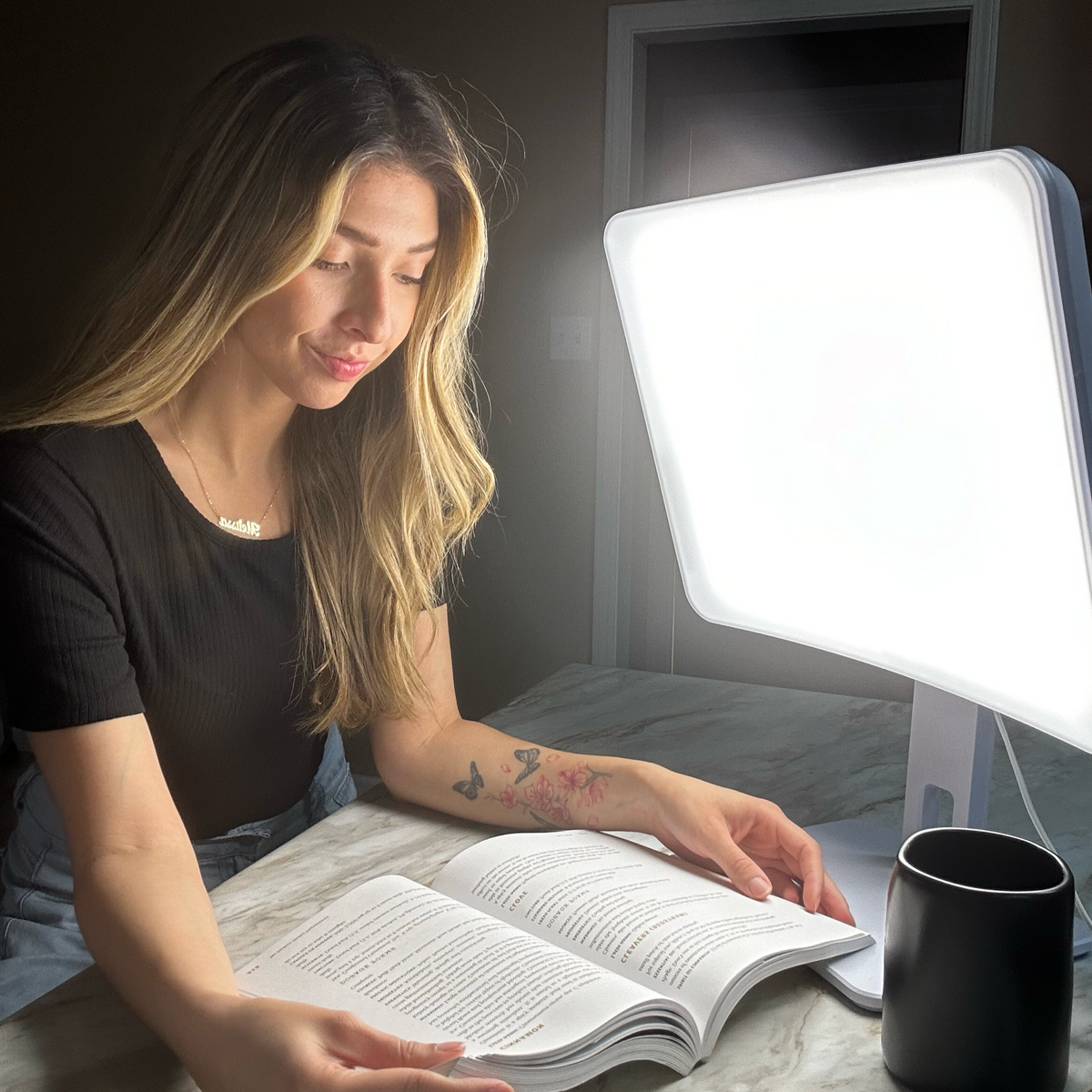 Woman reading a book under the Day-Light Elite 10,000 lux light therapy lamp
