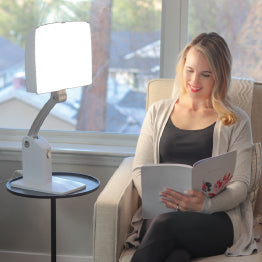 Woman reading a book in a chair in front of the Day-Light Sky light therapy lamp