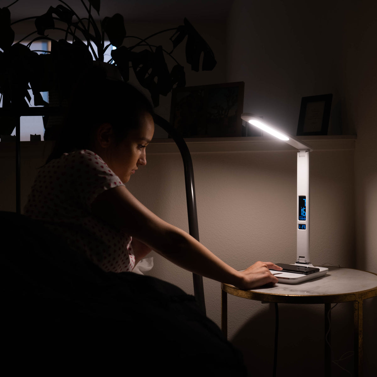 Woman turning on the TheraLite Radiance bedside lamp with wireless charger next to her bed